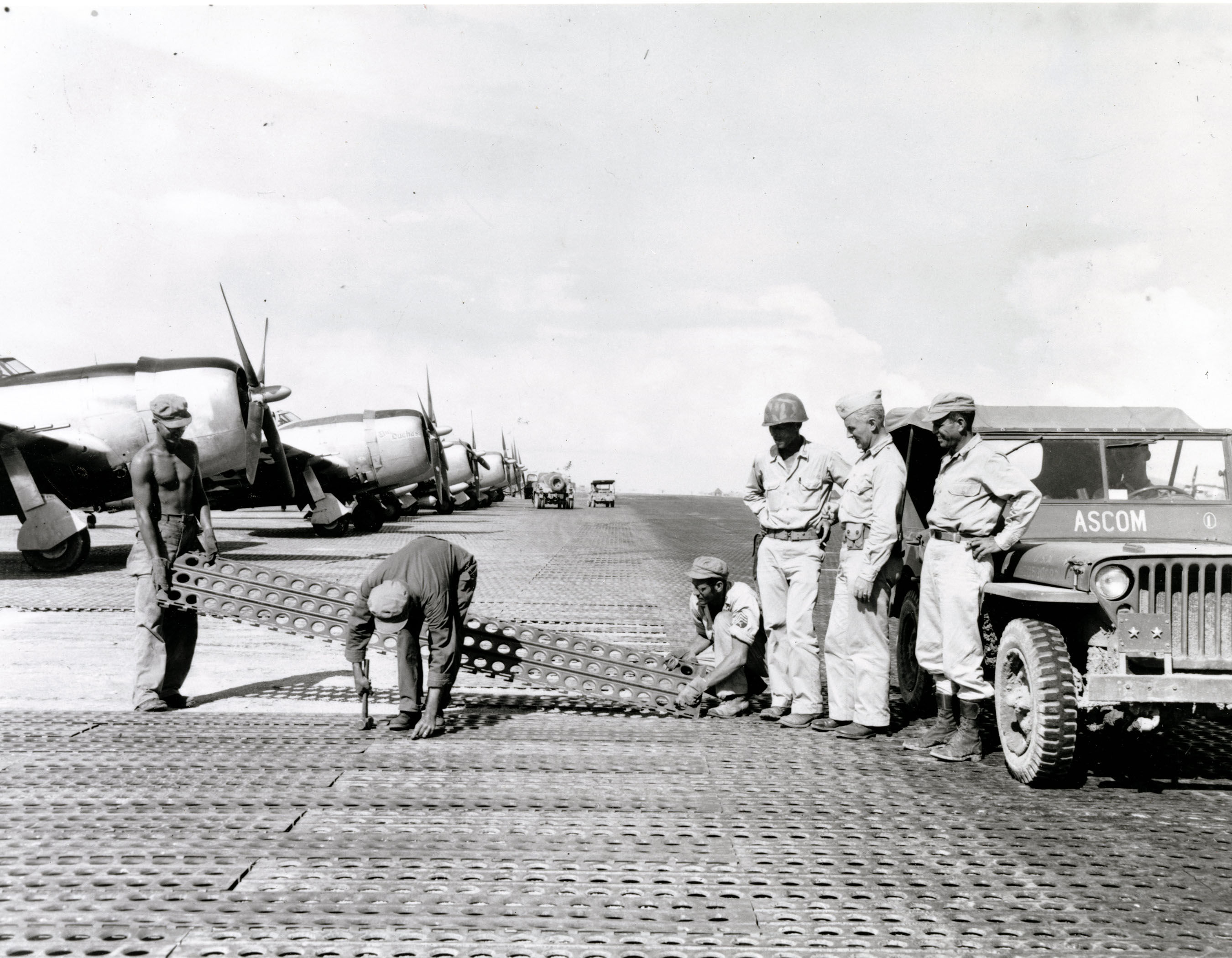 soldiers lay steel mats to create a runway as officers look on